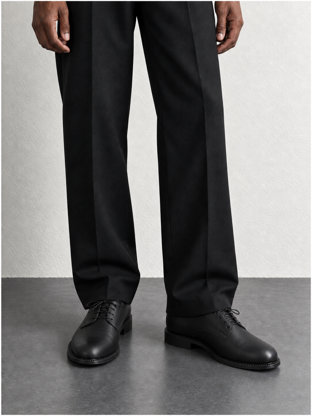 A close look at black tailored trouser hems and black leather derby shoes on a grey floor.