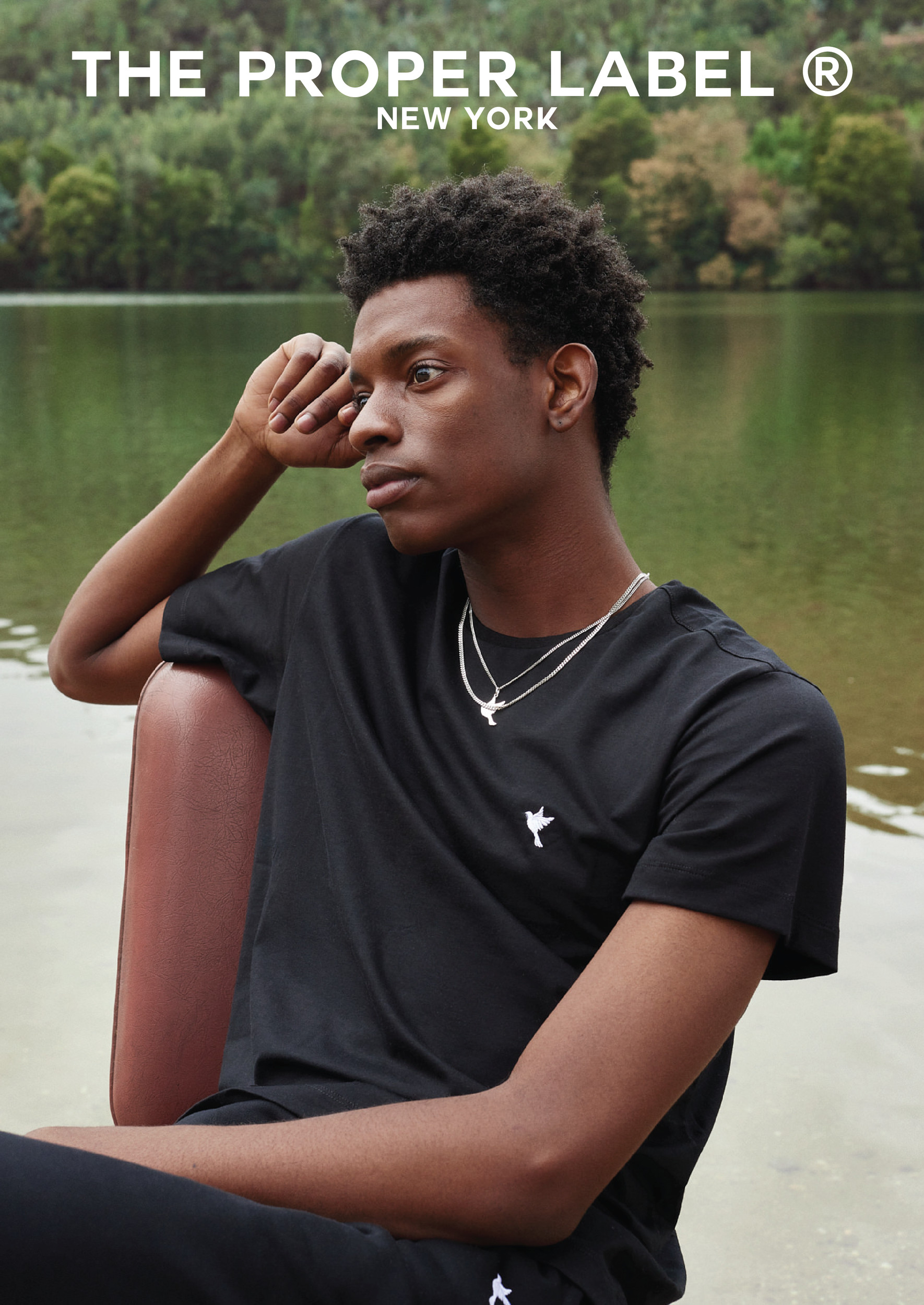 A seated model in a black T-shirt beside the water.
