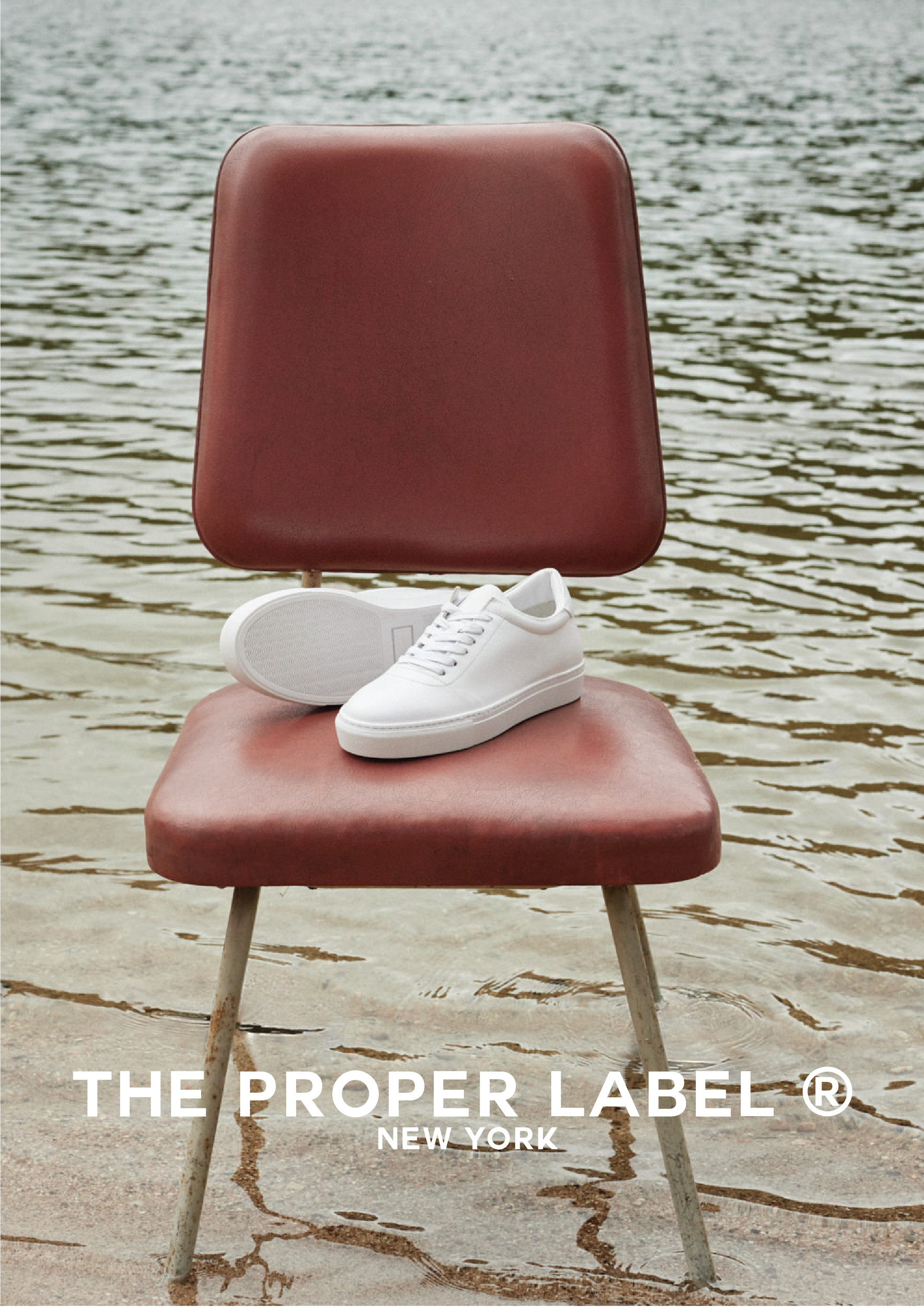 A white sneaker rests on a red chair at the water’s edge.